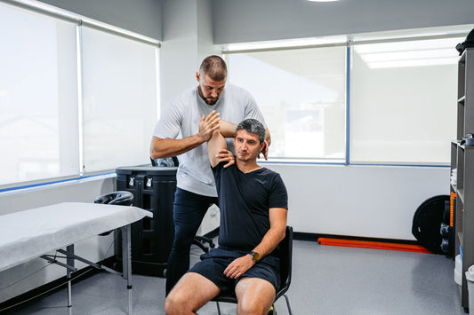 male athlete in black shirt working with athletic trainer to stretch out left arm