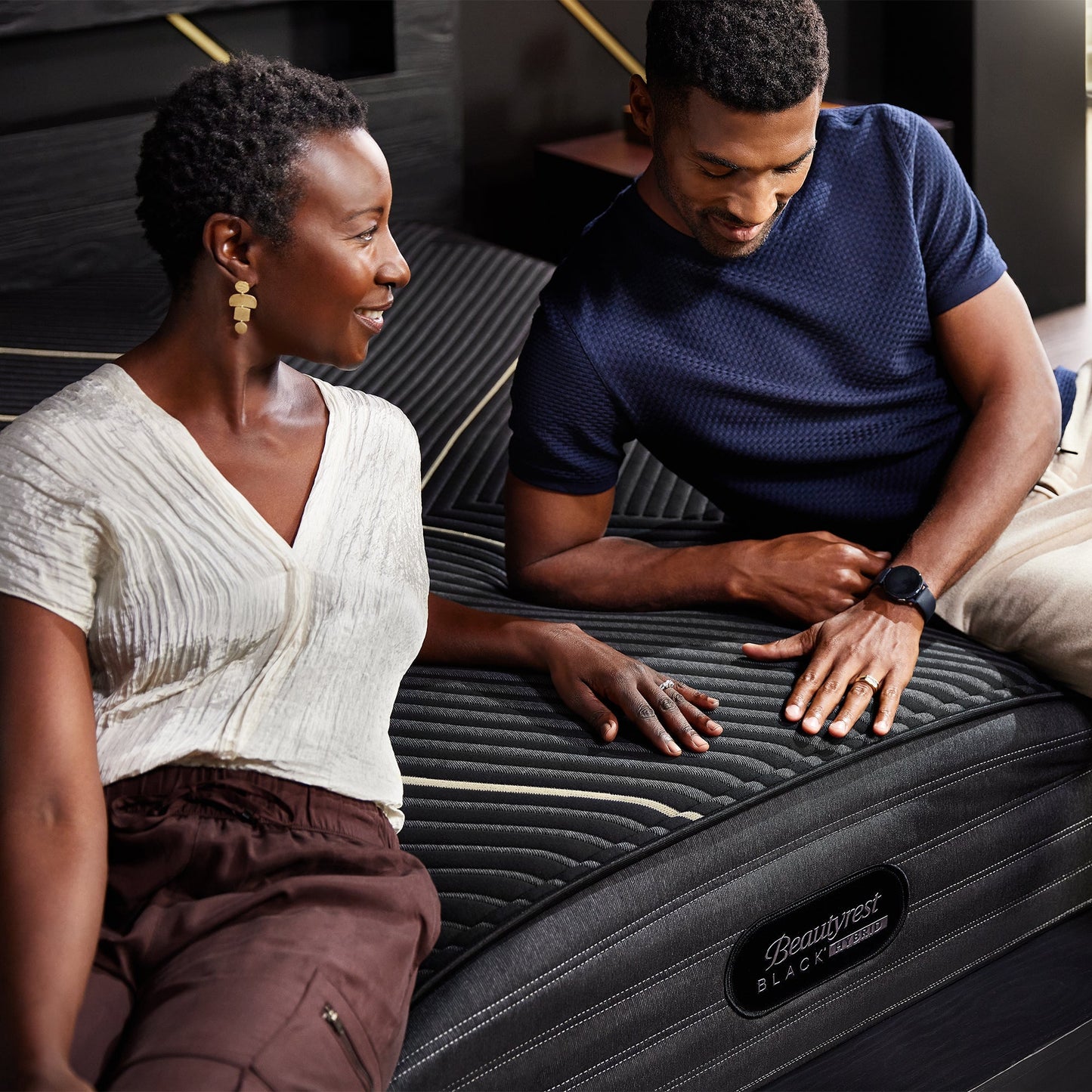 Couple Touches The Fabric Cover Of A Beautyrest Black Hybrid K-Class Firm Mattress
