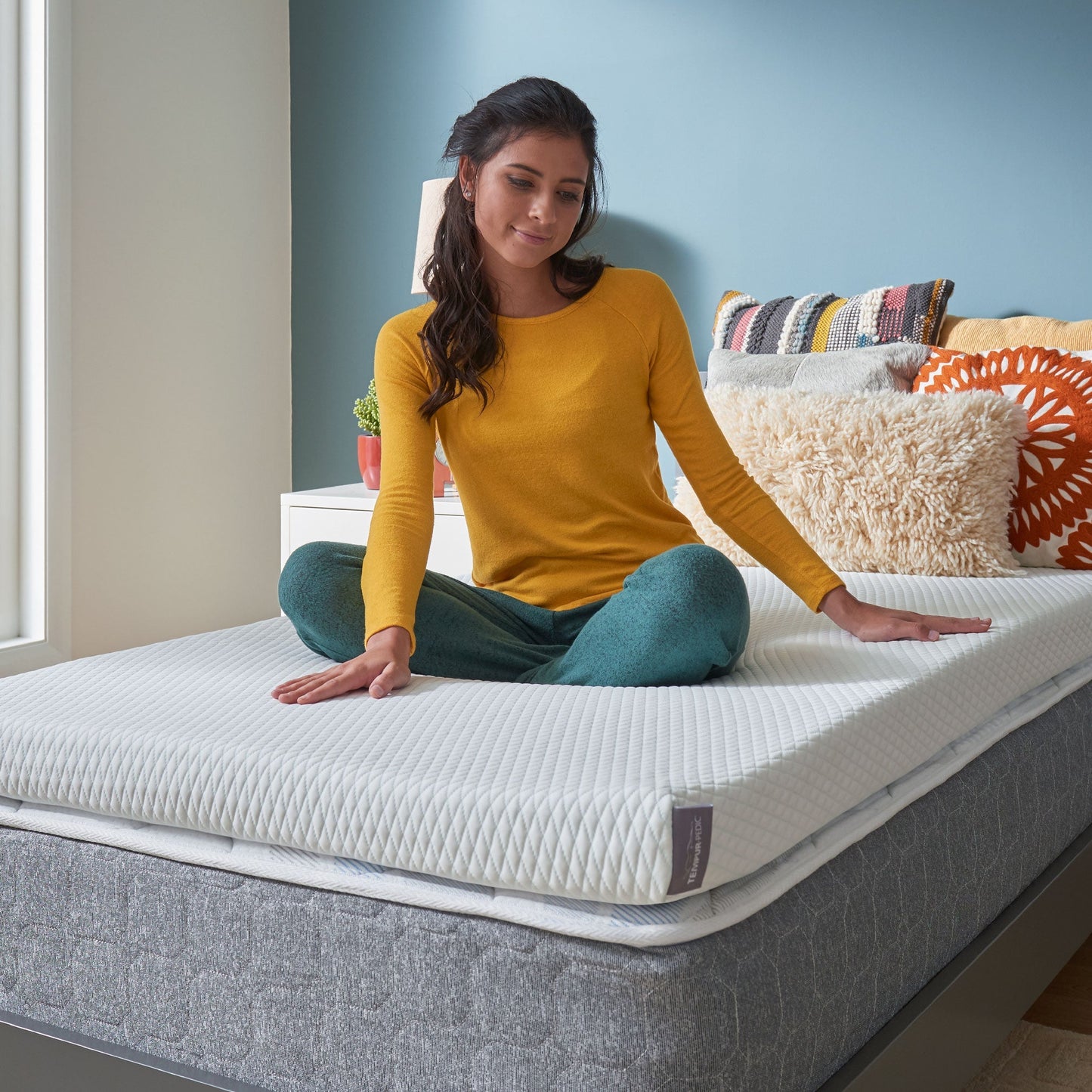Woman Sitting On A TEMPUR-Adapt® + Cooling Topper On Her Bed In Her Bedroom