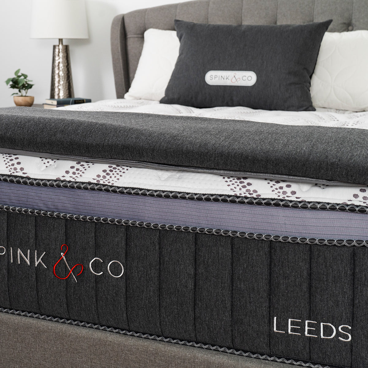 Spink & Co Leeds Luxury Firm mattress with gray throw blanket and pillows in clean modern bedroom. Closeup of hand stitched logo and bed name