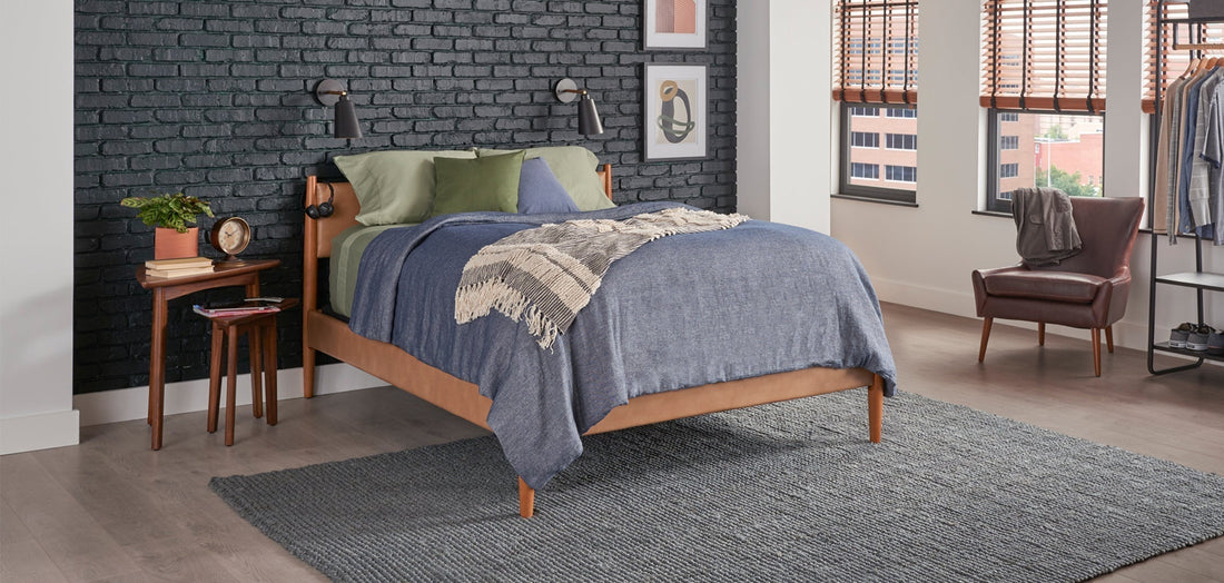 Bed with gray blanket and green accent pillows in a modern industrial bedroom