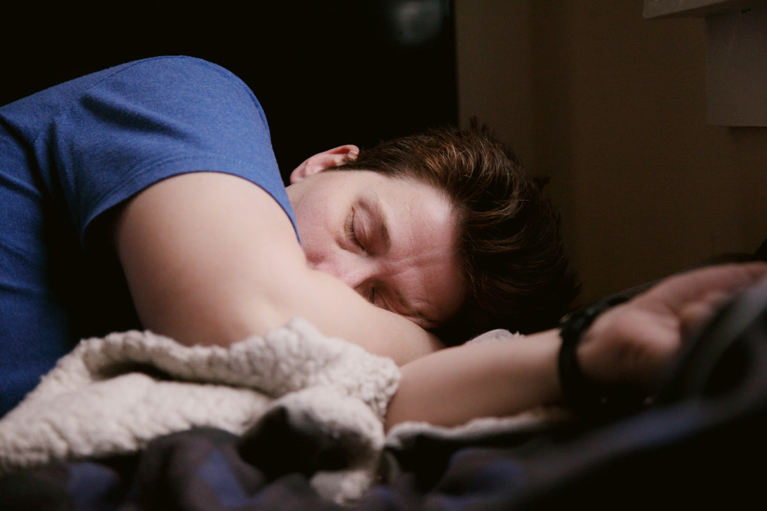 Man in a blue T-shirt sleeping on his side with his head on a pillow