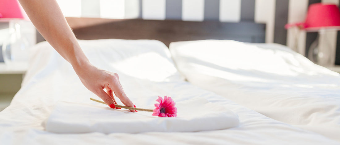 hand placing pink daisy on white sheets