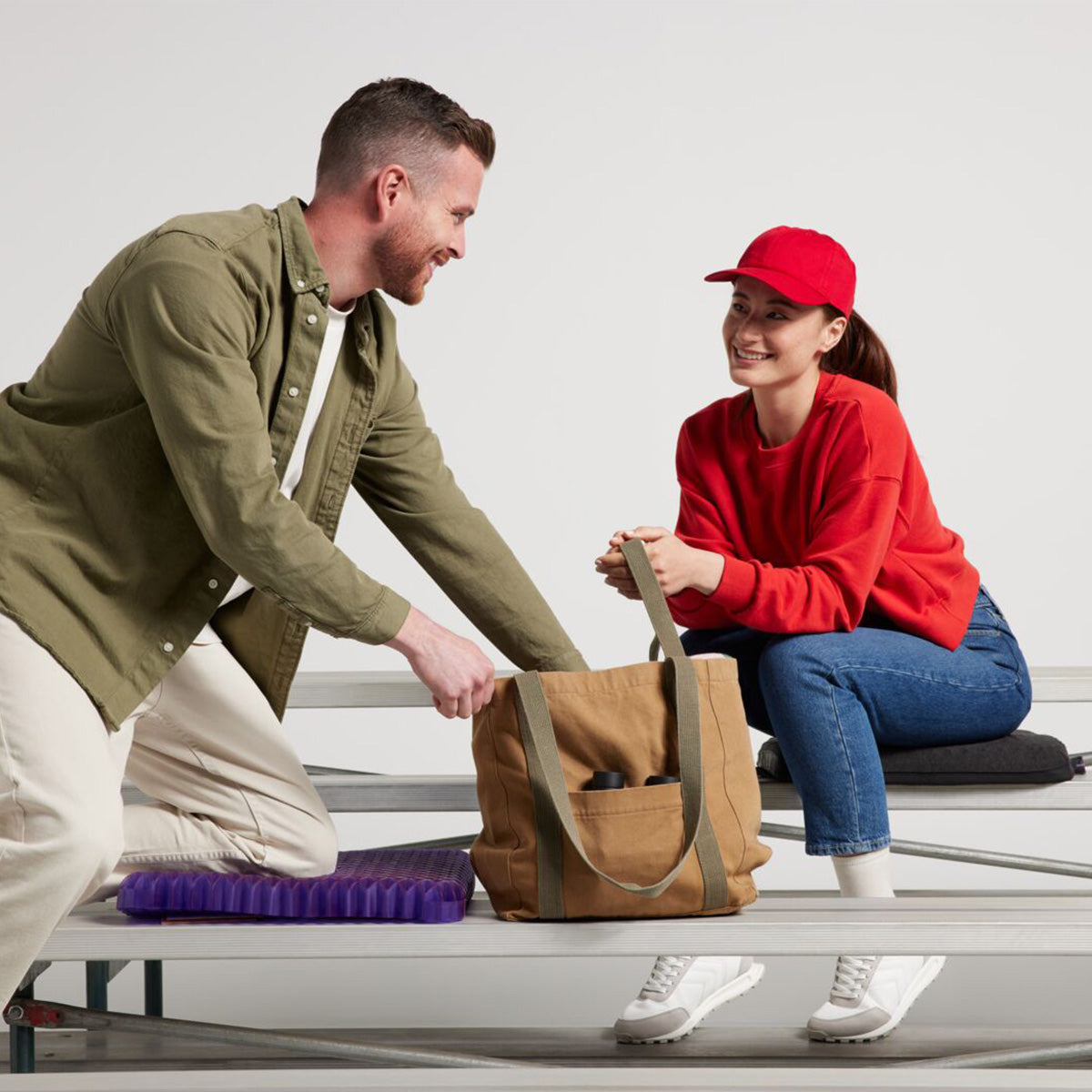 Man Kneeling and Woman Sitting On Purple Royal Seat Cushion At The Bleachers