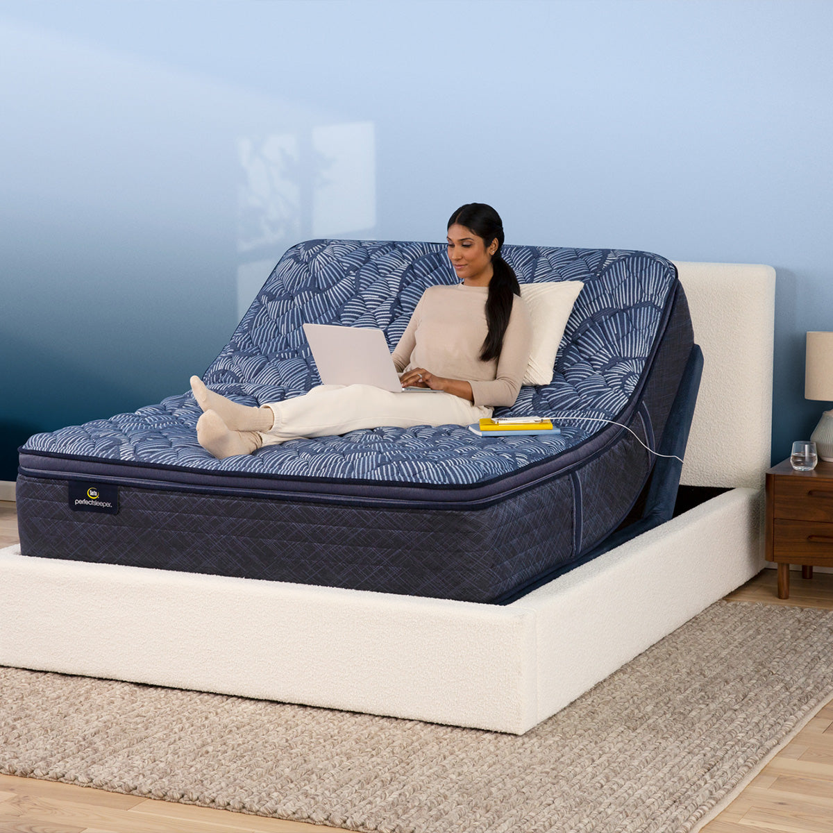 Woman using laptop on a mattress elevated by a Serta Motion Essentials Adjustable Base